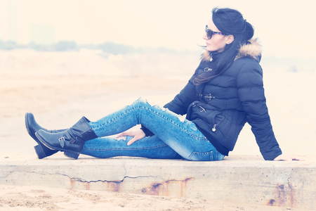 portrait of a woman with sunglasses at the beach sitting on a low wallの写真素材
