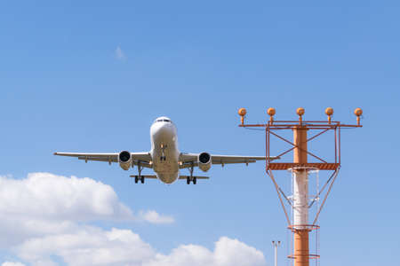Airplane approaching for landing on a sunny day. Airport aid instruments are visible in the image.