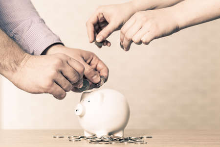Inserting a coin into a piggy bankの写真素材