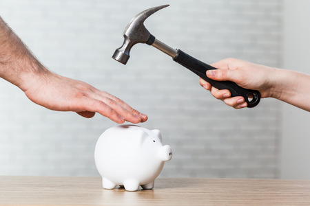 A hand holding a hammer which is raised above a white piggy bankの写真素材