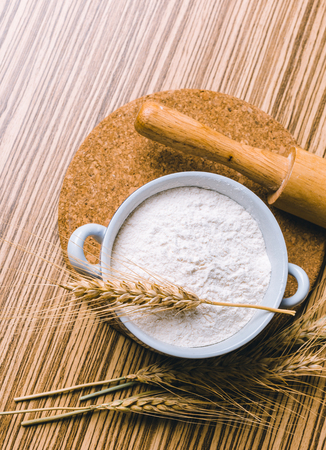 Flour in ceramic bowl with wheat on the wooden table closeup.