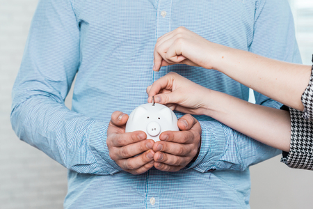 Inserting a coin into a piggy bankの写真素材