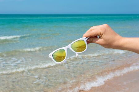 Sunglasses in hand on background of the beachの写真素材