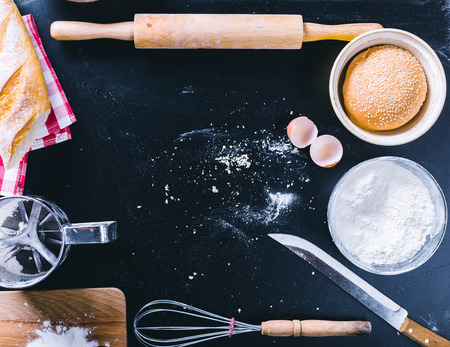 Baking dark background with blank cook book, eggshell, bread, flour, rolling pin. Ingredients for...