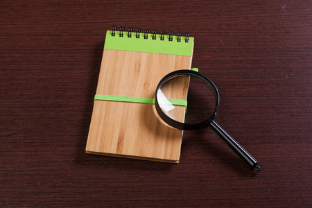 Notebook and magnifier on a wooden backgroundの写真素材