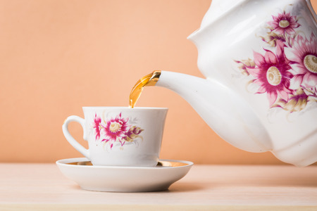 Old-style porcelain kettle pouring tea from jug to cup of teaの写真素材