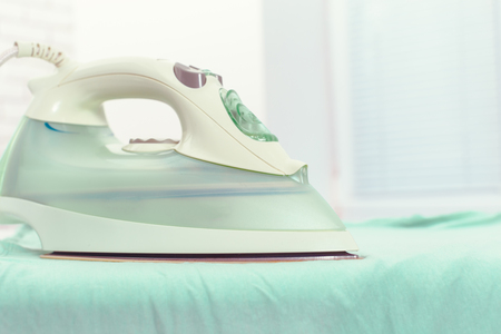 Iron on ironing board on light home interior backgroundの写真素材