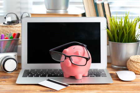 Piggy money box with laptop on wooden tableの写真素材