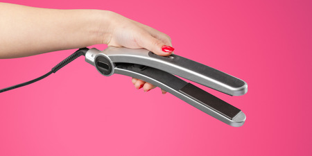 Woman hand with a hair iron isolated on a color backgroundの写真素材