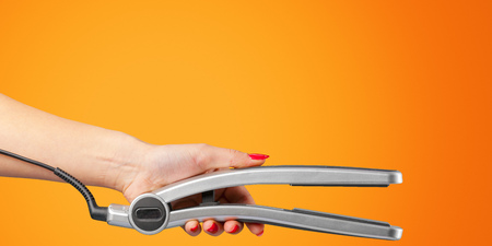 Woman hand with a hair iron isolated on a color backgroundの写真素材