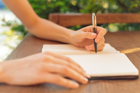 Woman hands making notes in a notepad on a cafe tableの写真素材