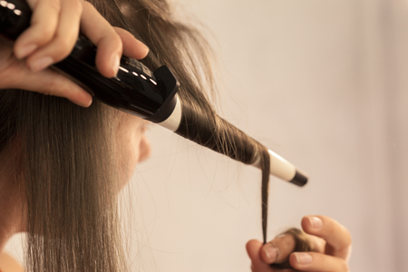 Hairstylist curling hair client in hairdressing salonの写真素材
