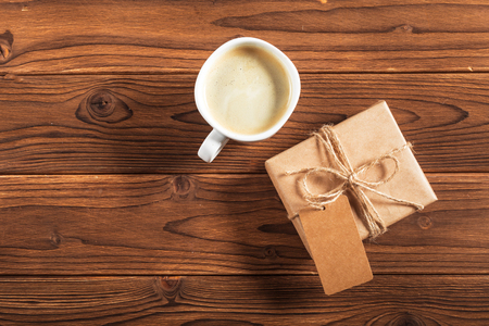 A cup of coffee and a wrapped gift on a wooden tableの写真素材