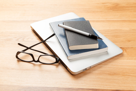 Notepad, pencil and glasses on the wooden background