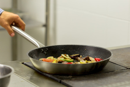 Chef frying vegetables on the gas stove with fire at the kitchenの写真素材