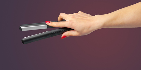 Woman hand with a hair iron isolated on a color backgroundの写真素材