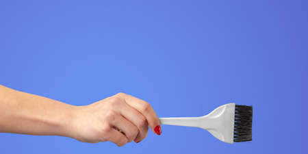 Woman hand with a hair dresser's tools and accessories isolated on color backgroundの写真素材