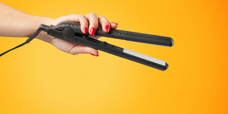 Woman hand with a hair iron isolated on a color backgroundの写真素材