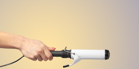 Woman hand with a hair styler isolated on color backgroundの写真素材