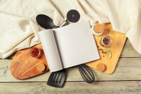 Blank sheet of opened notepad and kitchen utensils on  table with tablecloth, copy spaceの写真素材