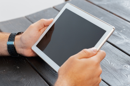 hands of a man holding tablet device over a wooden workspace table