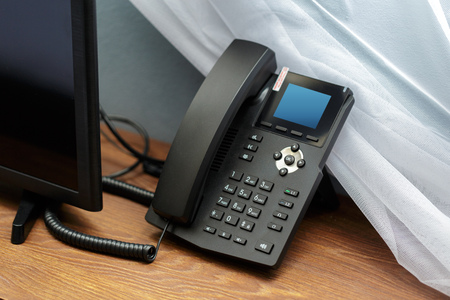 Closeup shot of a telephone receiver with buttons and texts on it in a hotel room.