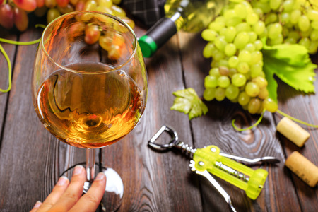 wine with branches of white grapes. On a wooden table.