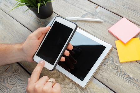 hands of a man holding tablet device over a wooden workspace tableの写真素材