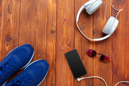 Sneakers and mobile phone with headphones on wooden tableの写真素材