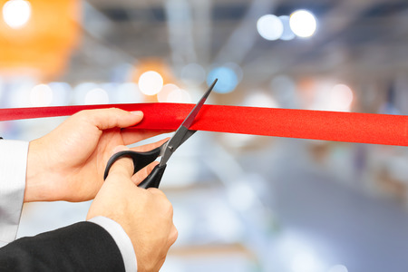 Businessman cutting red ribbon with pair of scissorsの写真素材