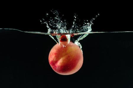 Peach dropped into water with bubblesの写真素材