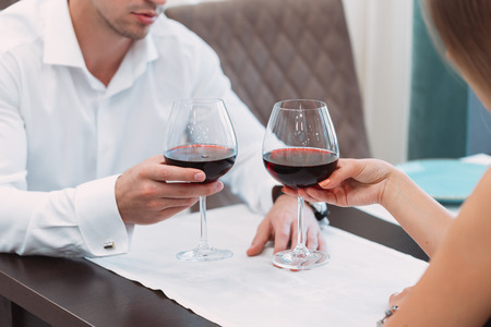 Beautiful young couple with glasses of red wine in luxury restaurantの写真素材