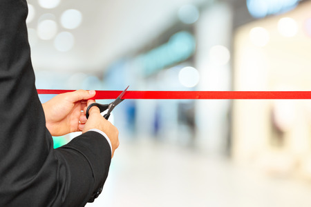 Businessman cutting red ribbon with pair of scissorsの写真素材