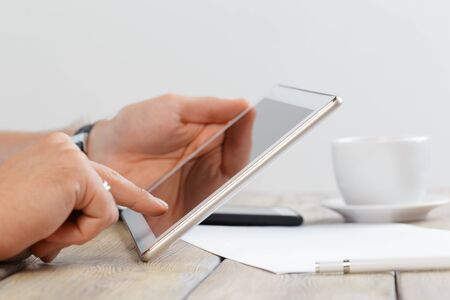 hands of a man holding tablet device over a wooden workspace tableの写真素材