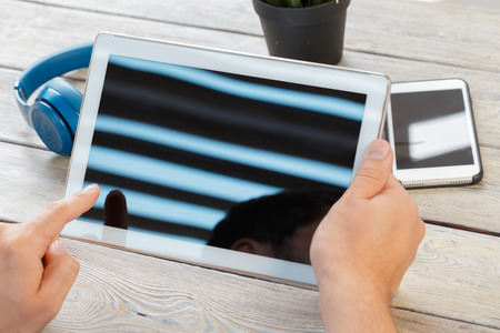 hands of a man holding tablet device over a wooden workspace table