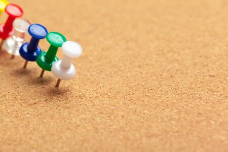 Group of thumbtacks pinned on corkboard in a row close up view