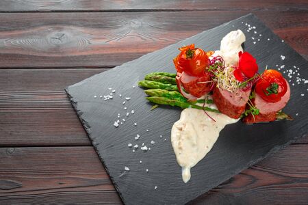 veal medallions with asparagus on black dishware , wooden table. creative photo.
