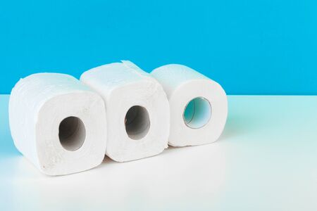 Three toilet paper rolls isolated on white table with blue background