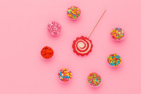 Lollipop and sugar sprinkles in paper bowls on pink background, top view. Creative photo.の写真素材