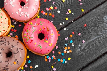 Assortment of colorful donuts decorated with colorful confetti sprinkles on dark wooden background. creative photo.の写真素材