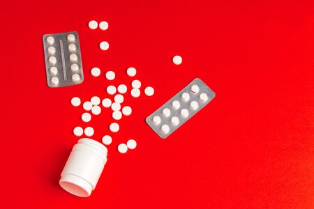 White pills spilling out of a toppled white bottle on red backgroundの写真素材