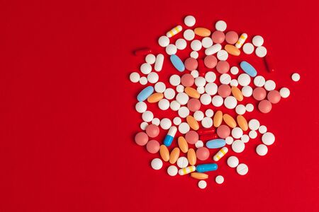 White pills spilling out of a toppled white bottle on red backgroundの写真素材