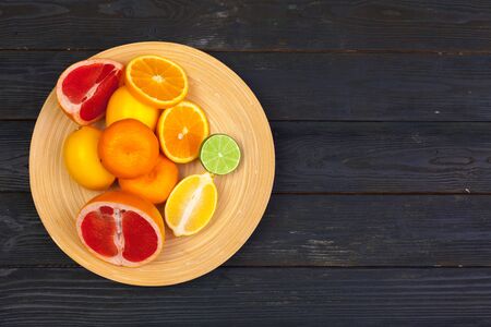 Bowl of citrus fruits on black wooden background, top view