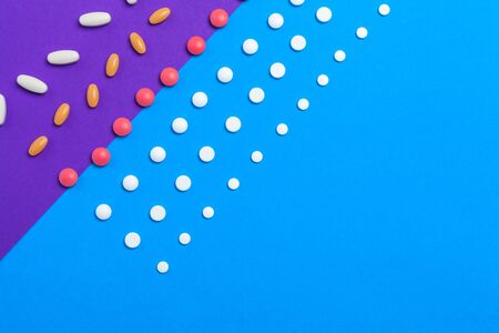 A pile of multicolored pills on blue background. Top view. Close up.