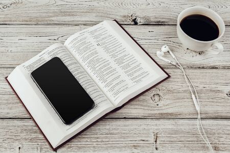Holy Bible and smartphone with black coffee cup on wooden background.の写真素材