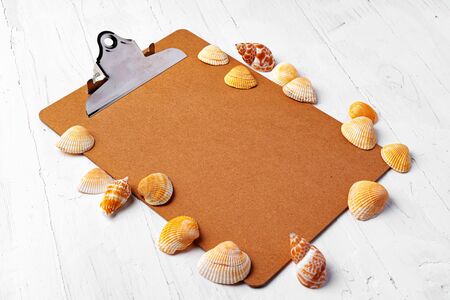Clipboard with sea shells on wooden table close up, copy space