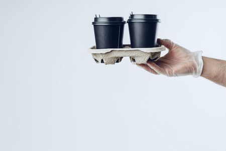 Man in medical gloves giving takeaway coffee cups. Safe service while covid-19 coronavirus pandemicの写真素材