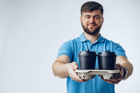 Man coffee shop worker giving takeaway cups of coffee on grey background