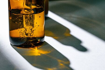 Brown glass bottles with oily skincare serum close up on white tableの写真素材