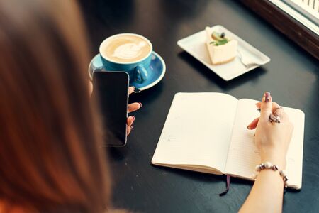 Young business woman sitting at the table in a coffee shop and making notes. Close up.の写真素材
